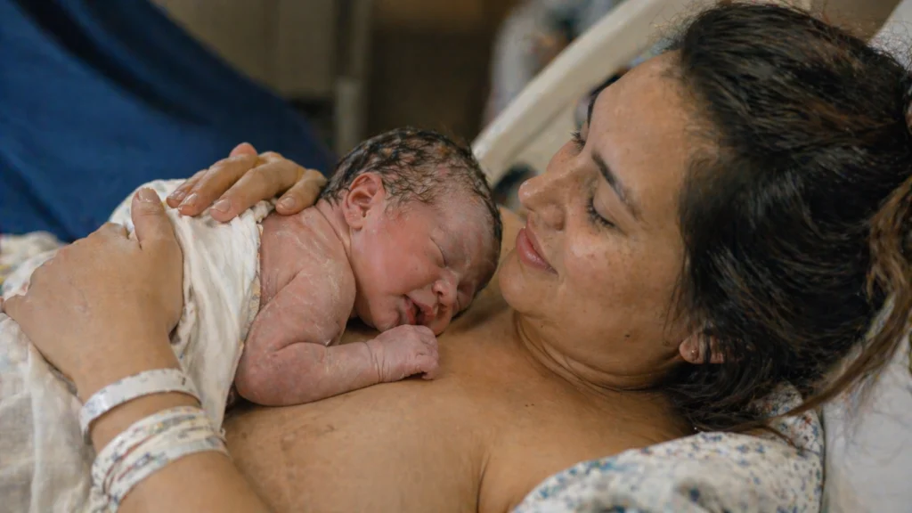 Madre sosteniendo a su bebé recién nacido en contacto piel con piel, representando el bonding y el vínculo afectivo desde el nacimiento. La escena muestra apego seguro, contacto emocional, cuidado materno y la importancia del contacto físico en el desarrollo psicológico y emocional del bebé.